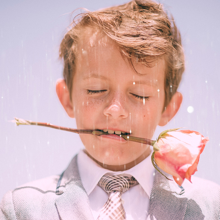 Nahaufnahme eines Jungen, der im Regen steht mit einer Rose zwischen den Zähnen.