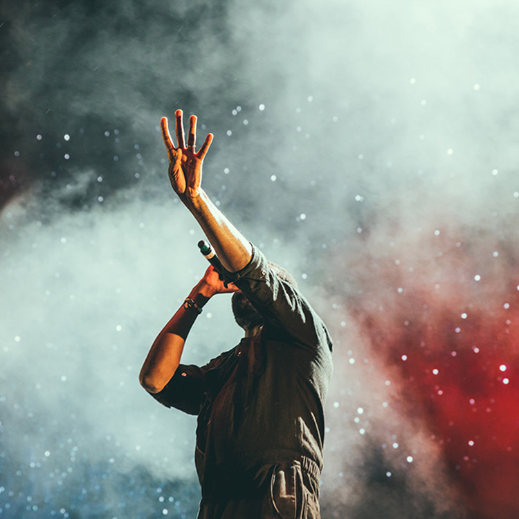 Sänger performt auf Bühne in Rauch und Konfetti und hält eine Hand in die Luft.