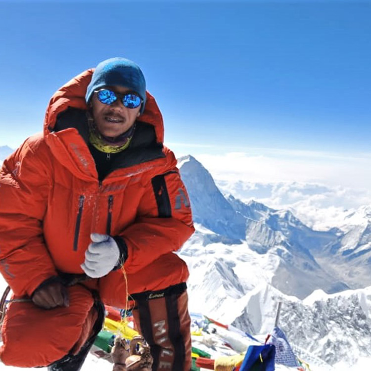 Sherpa auf dem Gipfel eines Berges mit Panorama im Hintergrund.